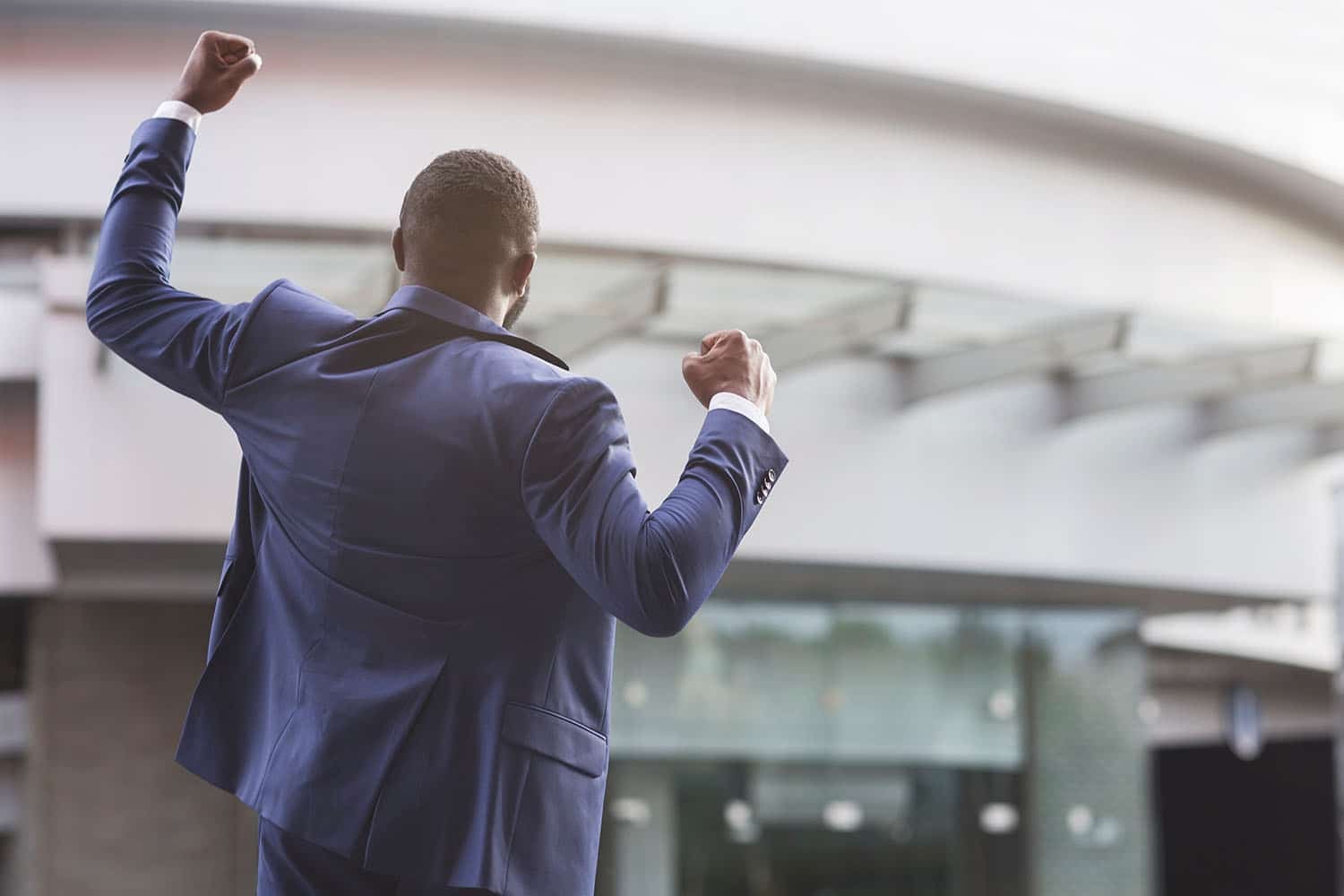 job seeker celebrating successful interview raising fists against business center, rear view with copy space